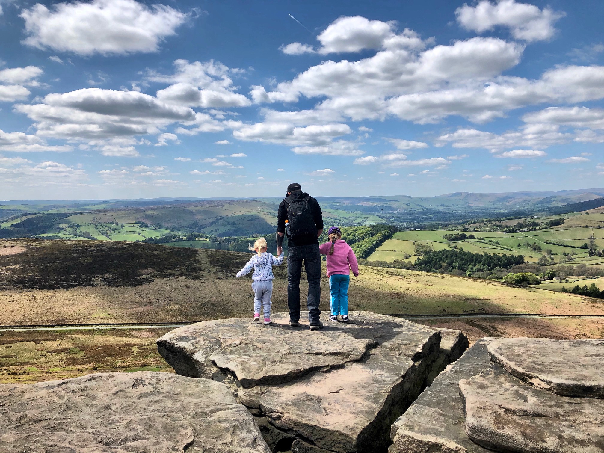 Family standing on the cliff edge of Stanage Edge, taking in stunning panoramic views over the Peak District moors and valleys